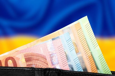 Bündel Euroscheine vor einer unscharfen Ukraine-Flagge