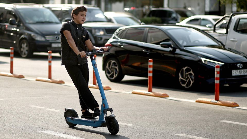 Ein Junge fährt mit einem E-Scooter an einer belebten Straße vorbei