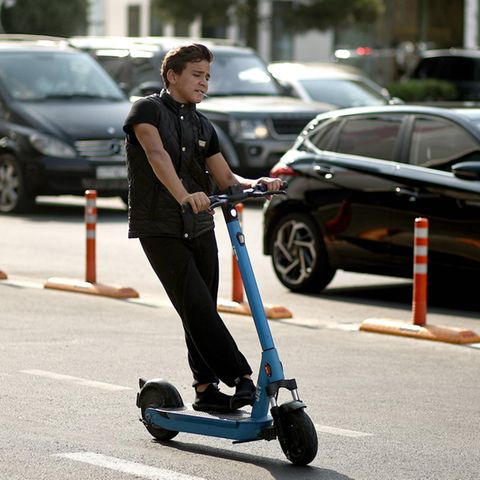Ein Junge brettert mit einem E-Scooter an einer dicht befahrenen Straße vorbei