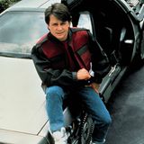 Michael J. Fox sitzt lässig auf dem Auto aus "Zurück in die Zukunft" und guckt in die Kamera