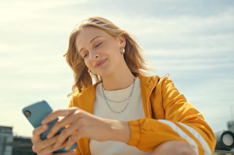 Tarif-Update bei Klarmobil: Junge Frau mit gelber Sportjacke sitzt im Freien und schaut auf ihr Handy