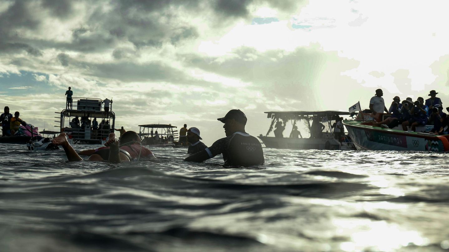 Strategiebeprechung auf dem Wasser, während Sonnenstrahlen durch die Wolken brechen. Carissa Moore (links) aus den Vereinigten Staaten spricht mit ihrem Trainer Shane Dorian während der ersten Runde im Surfen der Frauen.