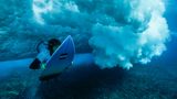 Die französische Athletin Johanne Defay taucht während eines Surftrainings unter einer brechenden Welle durch, um wieder rauszupaddeln. Das Wasser über dem Korallenriff ist zum Teil nur kniehoch.