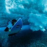 Die französische Athletin Johanne Defay taucht während eines Surftrainings unter einer brechenden Welle durch, um wieder rauszupaddeln. Das Wasser über dem Korallenriff ist zum Teil nur kniehoch.