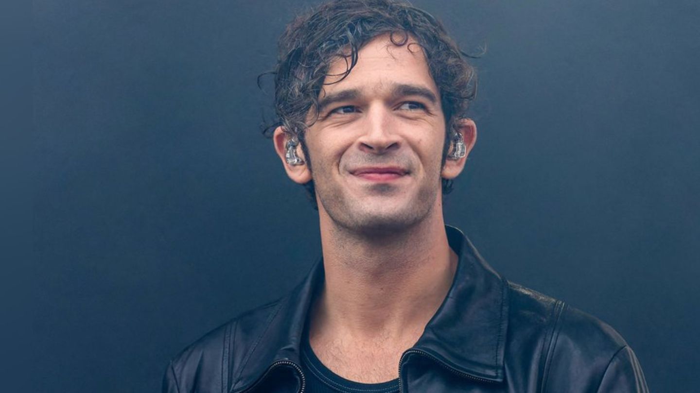 Matty Healy, Sänger der Band The 1975, steht mit Monitor-Kopfhörern auf der Bühne