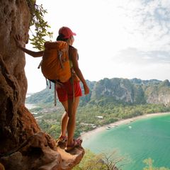 Reiseführer für Thailand: Eine Rucksacktouristin steht auf einem Berg und schaut auf das Meer.