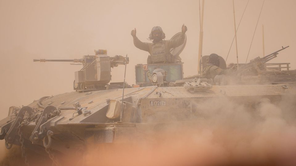 An Israeli soldier gives a thumbs up while standing on a battle tank