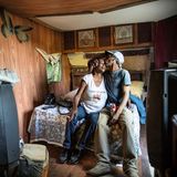 Ein Ehepaar sitzt auf dem Bett in einem robusten, Holz verkleideten Schlafzimmer. Der Mann küsst seine Frau auf die Stirn.