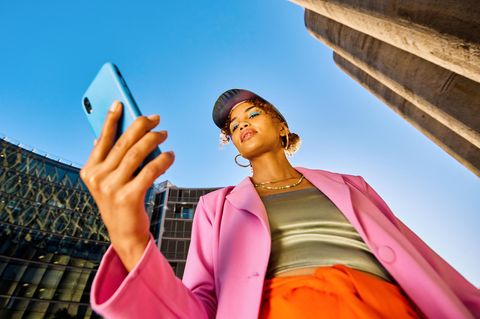 eine Modebewusste Frau steht mit ihrem Handy in der Innenstadt und schaut auf den Display
