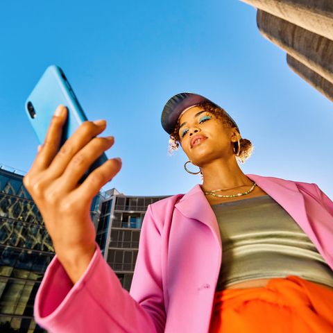 eine Modebewusste Frau steht mit ihrem Handy in der Innenstadt und schaut auf den Display