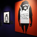 Der Planet der Affen  Was sehen wir? 2002 sprayte Banksy diesen sinister dreinblickenden Schimpansen zum ersten Mal in Brighton auf eine Hauswand, mit wechselnden Sprüchen wie "Keep It Real" auf der Reklametafel, die der Affe um seinen Hals trägt. Im Lauf der Jahre wurde er in seiner obigen Form zu einem der beliebtesten und bekanntesten Banksy-Motive.  Was will uns Banksy damit sagen? Diesmal ließ Banksy daran keinen Zweifel, der Schimpanse macht ja dafür Reklame. Übersetzt heißt der Slogan: "Lacht nur, aber eines Tages haben wir das Sagen."