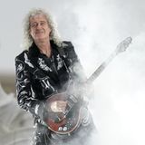 Brian May steht mit einer Gitarre im Rauch.