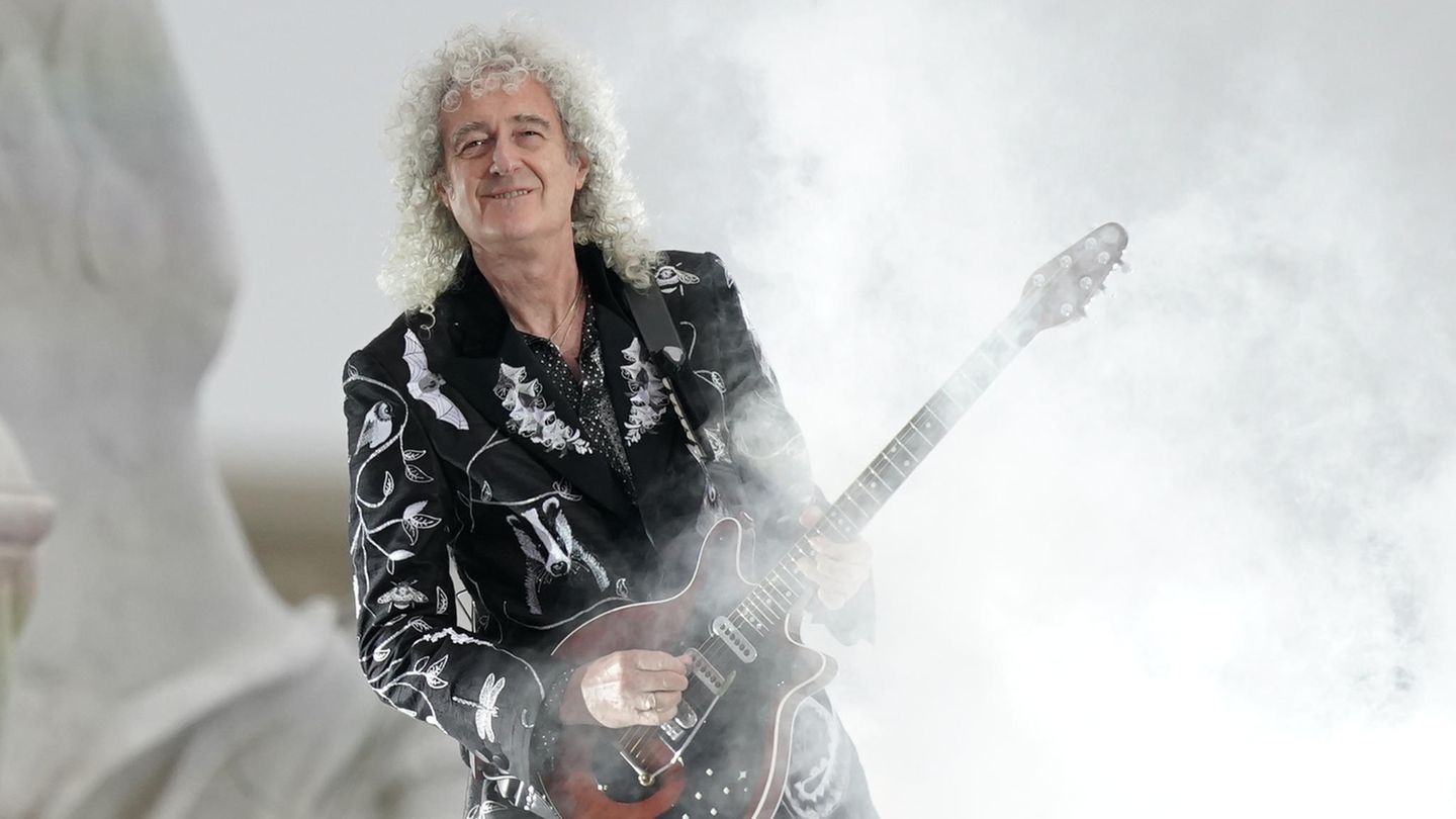 Brian May steht mit einer Gitarre im Rauch.