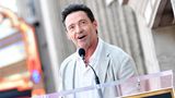 Hugh Jackman schaut an der Kamera vorbei und spricht in ein Mikro.