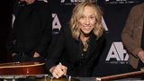 Sheryl Crow schreibt auf eine Gitarre und lächelt in die Kamera.