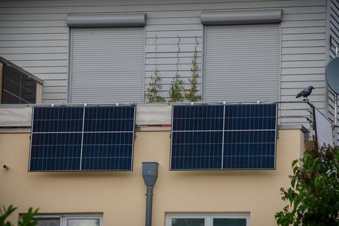 Zwei Balkonkraftwerke an der Balustrade, im Hintergrund zwei Fenster mit geschlossenen Rollläden.