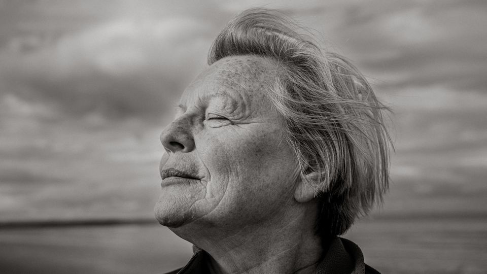 Joy Milne steht mit geschlossenen Augen am Strand und dreht den Kopf seitlich