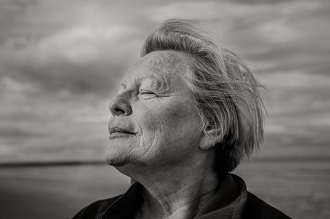 Joy Milne steht mit geschlossenen Augen am Strand und dreht den Kopf seitlich