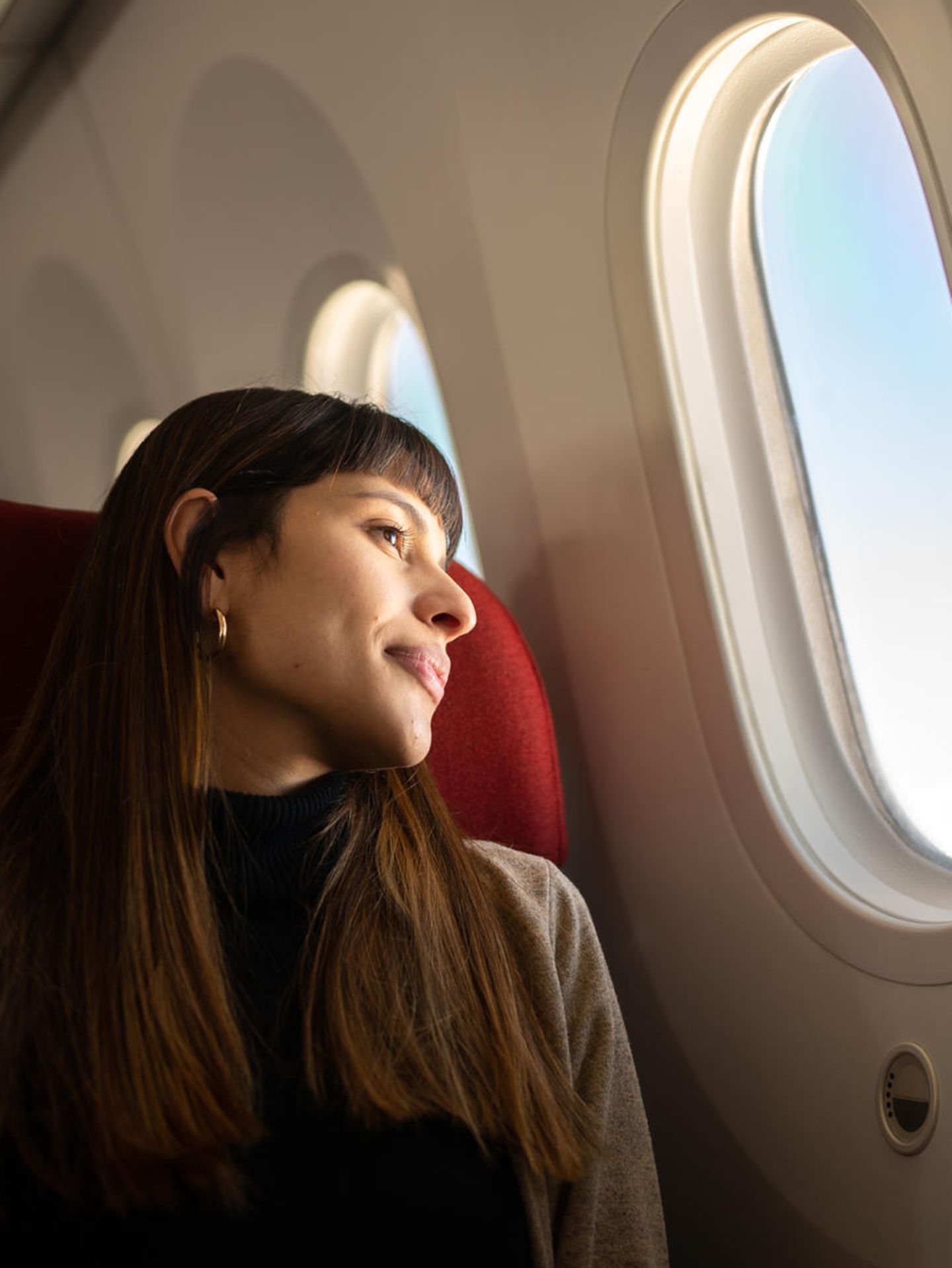 Tipps für Langstreckenflüge: Eine Frau zieht im Flugzeug und schaut aus dem Fenster.