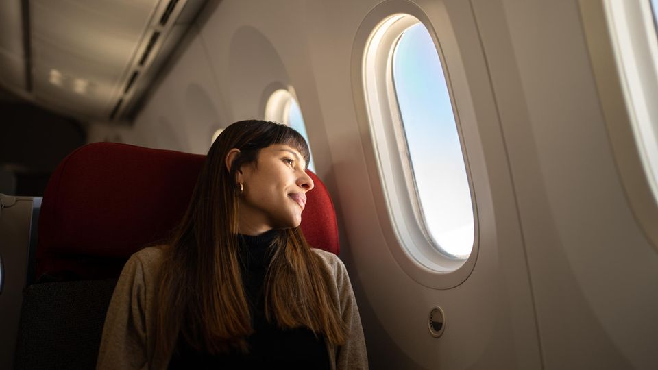 Tipps für Langstreckenflüge: Eine Frau zieht im Flugzeug und schaut aus dem Fenster.