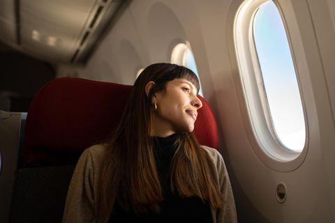 Tipps für Langstreckenflüge: Eine Frau zieht im Flugzeug und schaut aus dem Fenster.