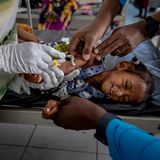 Ein kleines Kind liegt auf einem Tisch, mehrere Hände ragen ins Bild und versorgen das Kind medizinich