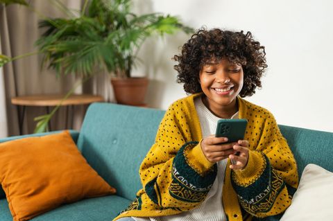 Mega SIM: Junge Frau sitzt auf der Couch und guckt lachend auf ihr Smartphone.