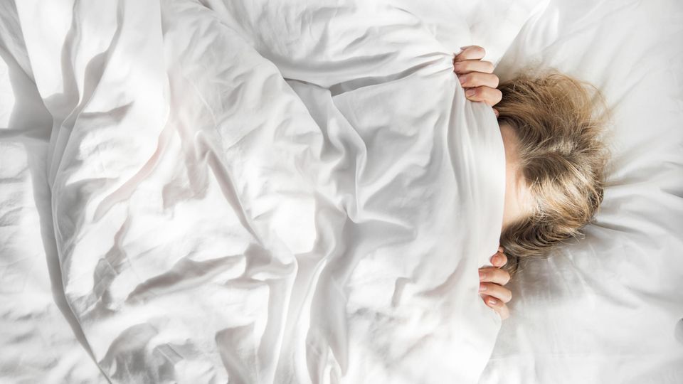 Im Morgenlicht zieht sich eine Frau im Bett die Decke übers Gesicht