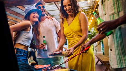 Grillfest: Eine Gruppe von Freunden steht um einen Grill und lacht miteinander.