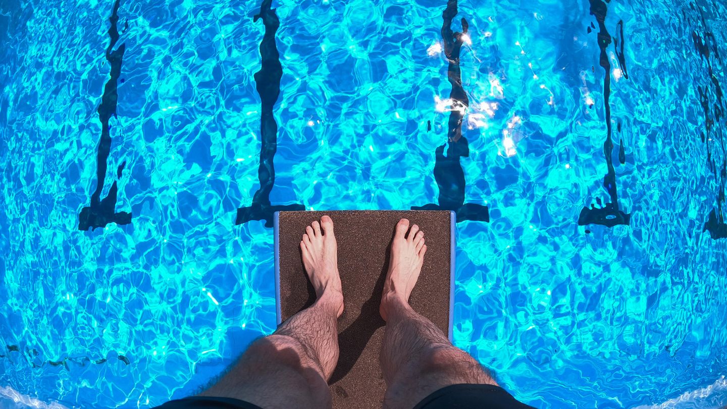 Ein Mann steht auf einem Zehn-Meter-Brett und schaut hinab aufs Wasser des Freibades