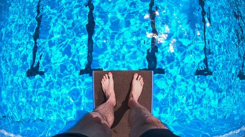 Ein Mann steht auf einem Zehn-Meter-Brett und schaut hinab aufs Wasser des Freibades