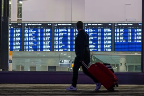 Ein Mann mit Koffer läuft an einer Anzeigetafel für die Abflüge am Flughafen München vorbei