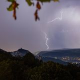 Blick von erhöhter Position über den Rhein, im Hintergrund schlagen Blitze in die Landschaft ein