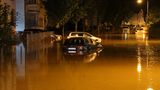 Eine Straße steht komplett etwa 50 Zentimeter unter Wasser, zu sehen sind parkende Autos und ein Motorad