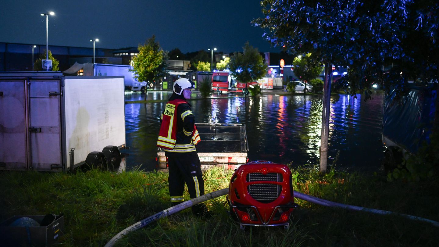 Ein Feuerwehrmann steht neben einer roten Pumpe, vor ihm der Parkplatz an der überfluteten Tankstelle in Aurich
