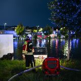 Ein Feuerwehrmann steht neben einer roten Pumpe, vor ihm der Parkplatz an der überfluteten Tankstelle in Aurich