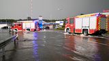 Zwei Feuerwehrautos fahren über ein überflutetes Tankstellen-Grundstück
