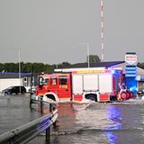Zwei Feuerwehrautos fahren über ein überflutetes Tankstellen-Grundstück