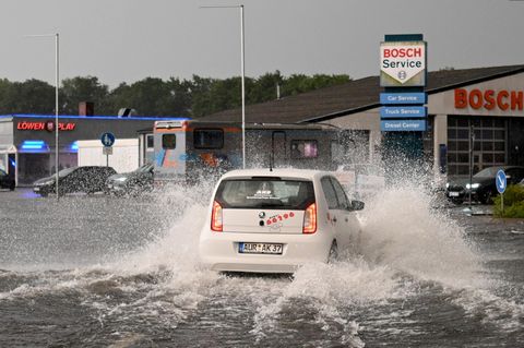 Ein Auto fährt durch eine großw Wasserpfütze, Gewitter sorgten in Deutschland für Überschwemmungen.