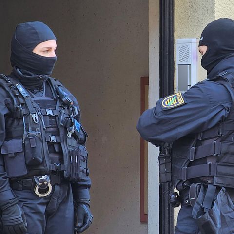 Zwei vermummte Polizisten stehen während einer Wohnungsdurchsuchung an einer Haustür
