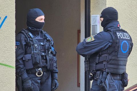 Zwei vermummte Polizisten stehen während einer Wohnungsdurchsuchung an einer Haustür