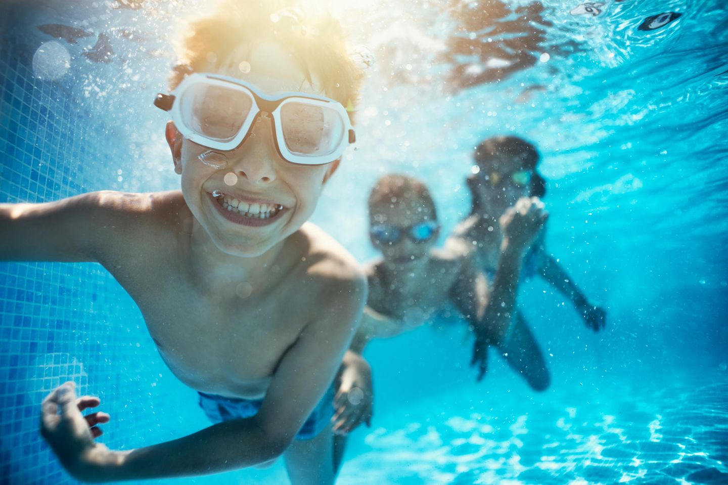 Ein Junge mit Schwimmbrille taucht in einem Pool im Freibad