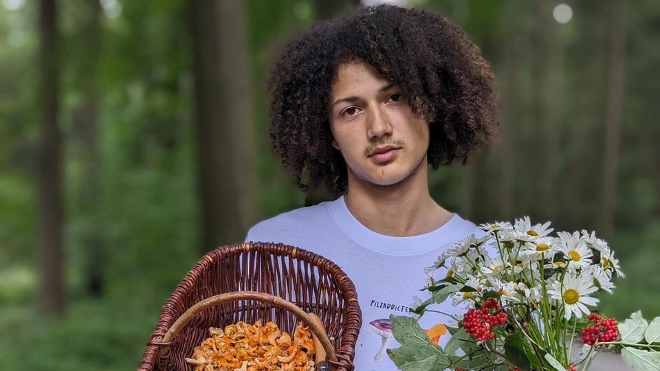 Pilzexperte Tristan Jurisch hält einen Korb mit Pfifferlingen und einen Blumenstrauß.