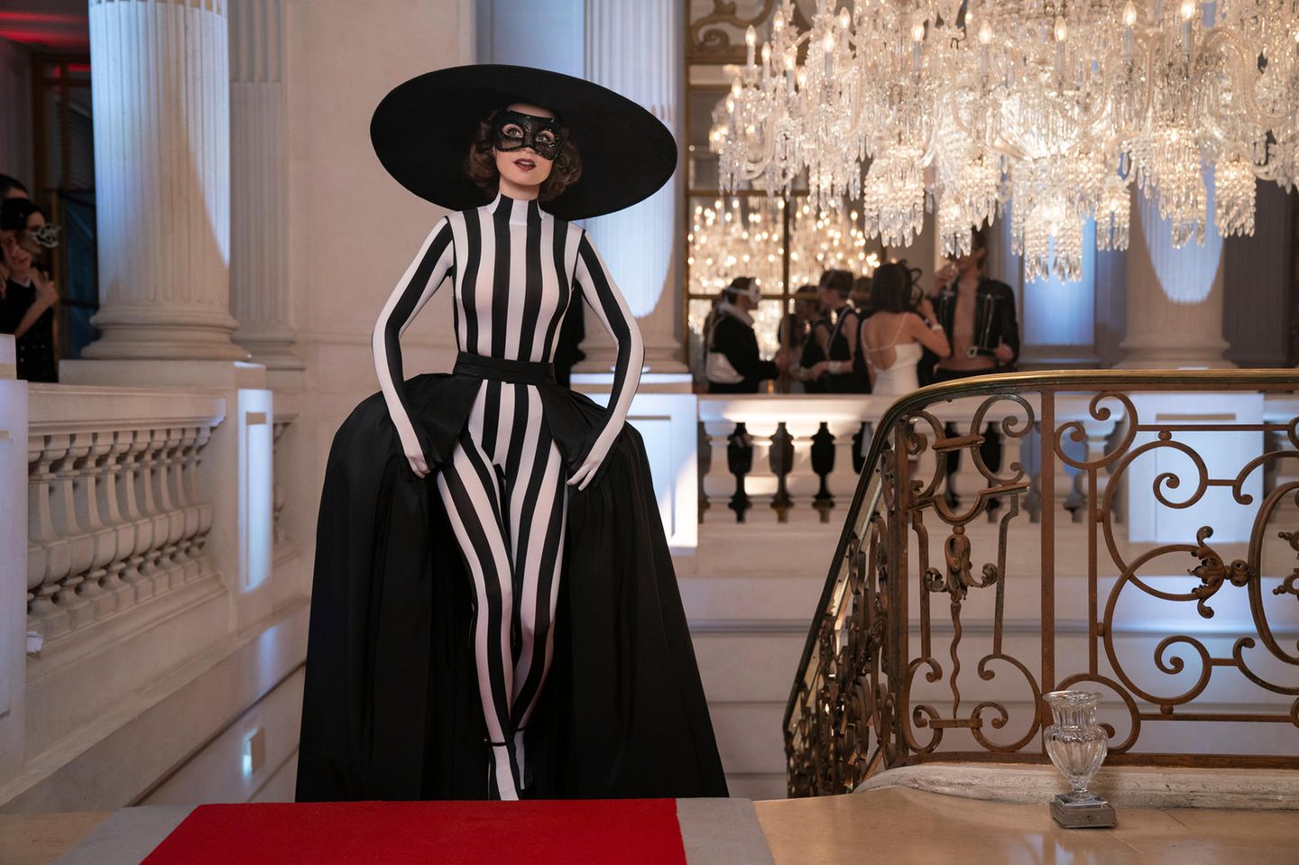 ... sind zahlreiche Outfits trotzdem. Aber dann mit Ansage: Hier besucht Emily einen Maskenball mit Schleppe, Jumpsuit und einem Hut, der so riesig ist, dass sie beim Drehen auf eine eigentlich geplante Szene im Taxi verzichten mussten. Das Ungetüm aus dem Haus der italienisch-französischen Designerin Nina Ricci passte einfach nicht rein.