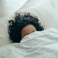 Schlafstörung: Eine junge Frau mit dunklen lockigen Haaren liegt im Bett