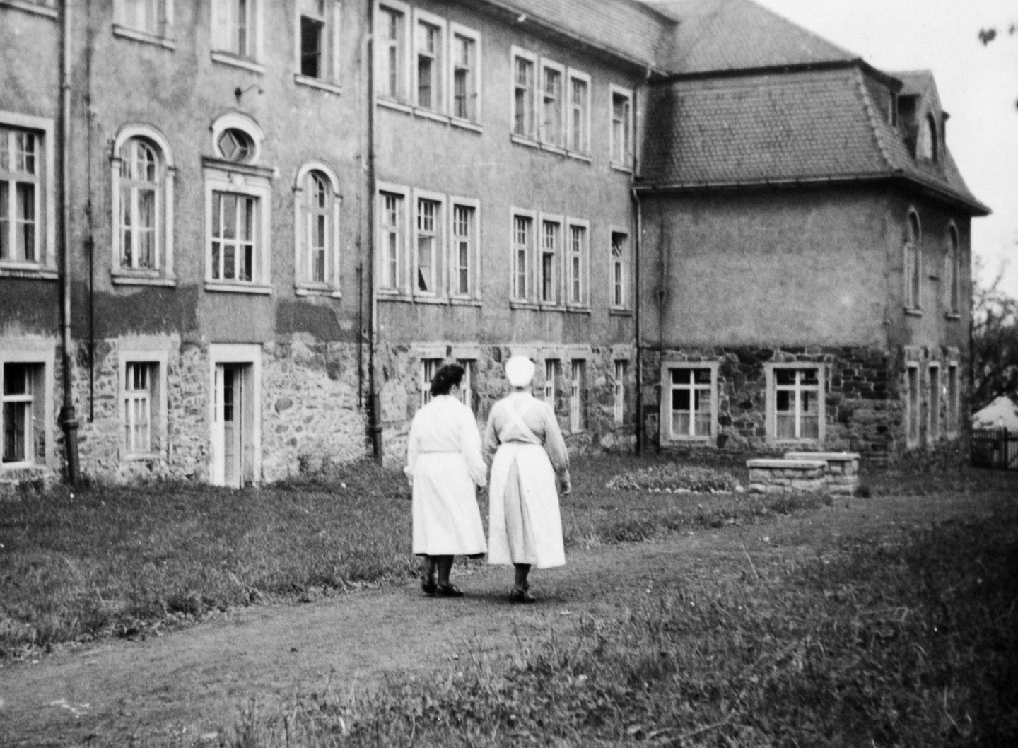 DDR: Zwei Krankenschwestern gehen entlang einer "Tripperburg"