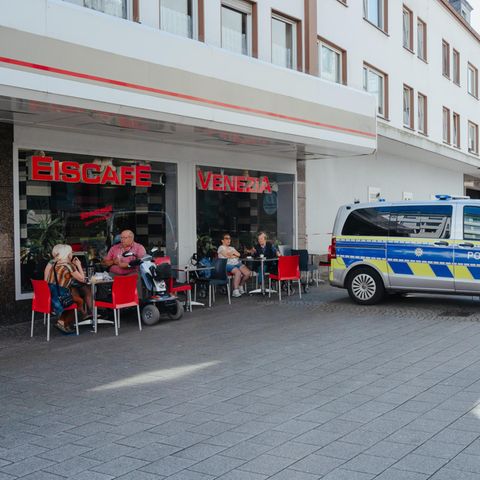 Gäste sitzen vor einem Solinger Eiscafé, ein Polizeiauto steht davor