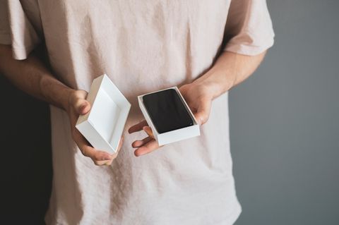 Handytarif mit oder ohne Smartphone: Hände halten eine geöffnete Verpackung mit Smartphone.