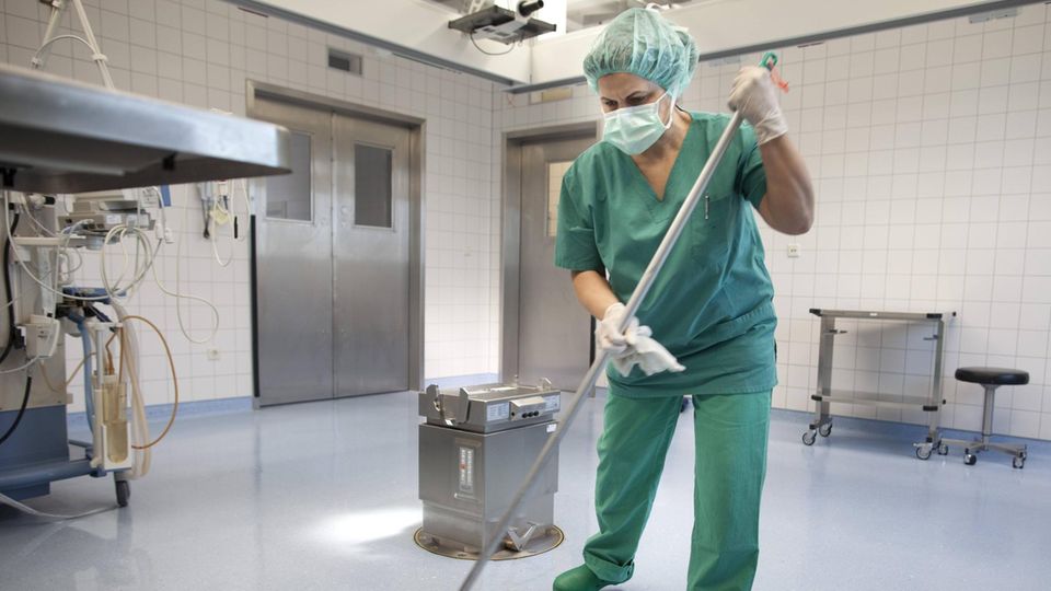 Eine Frau wischt einen OP-Saal, mit Haarnetz, Mundschutz und Handschuhen; Symbolbild Reinigungskraft OP