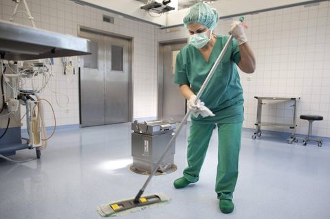 Eine Frau wischt einen OP-Saal, mit Haarnetz, Mundschutz und Handschuhen; Symbolbild Reinigungskraft OP